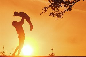 Man Lifting a Child in the Air in Front of a Sunset