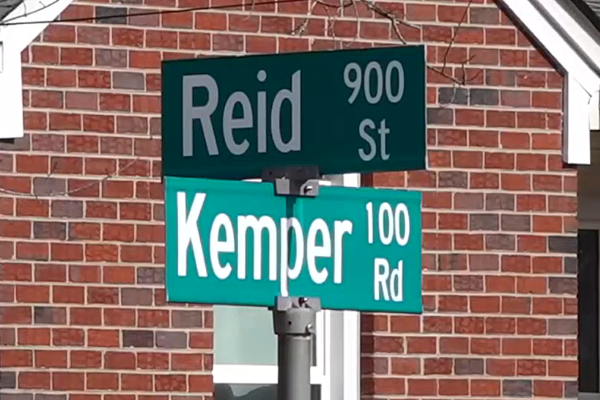 Kemper 100 Rd sign and Reid 900 St sign in front of a brick house.